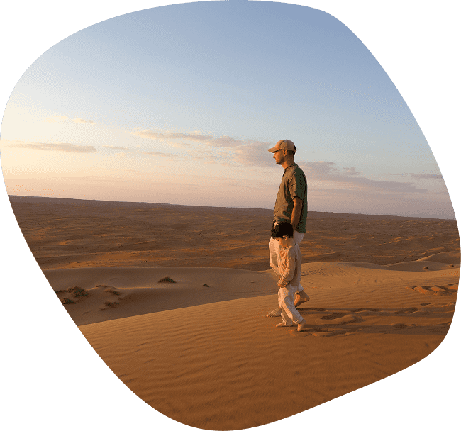 Homme marchant avec un enfant dans le désert de Wahiba Sands à Oman au coucher du soleil