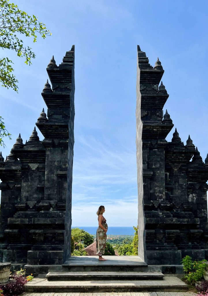 Femme face à un temple balinais traditionnel avec vue sur la jungle et l’océan à Bali